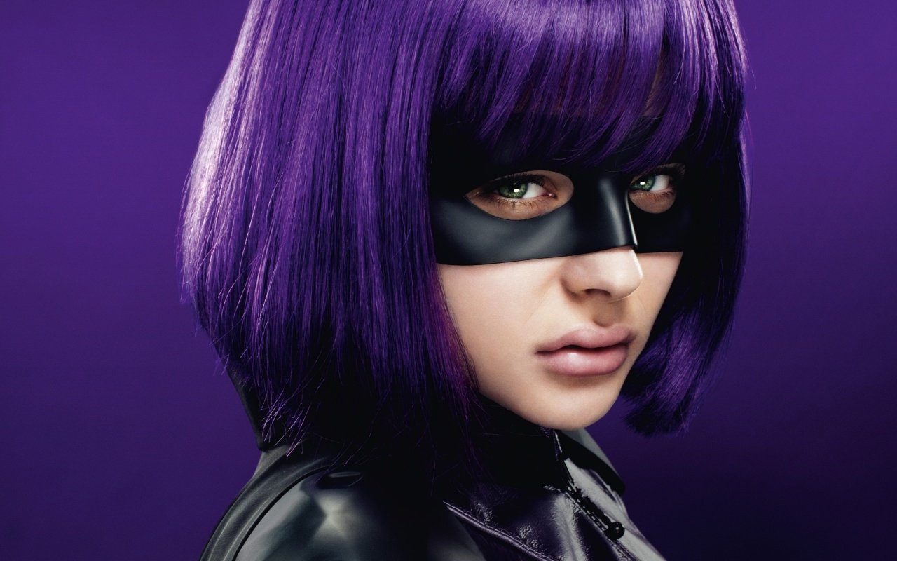 Chloë Grace Moretz as Hit-Girl in Kick-Ass 2, showcases her striking purple hair and masked look in a dramatic close-up against a sleek black and purple backdrop.