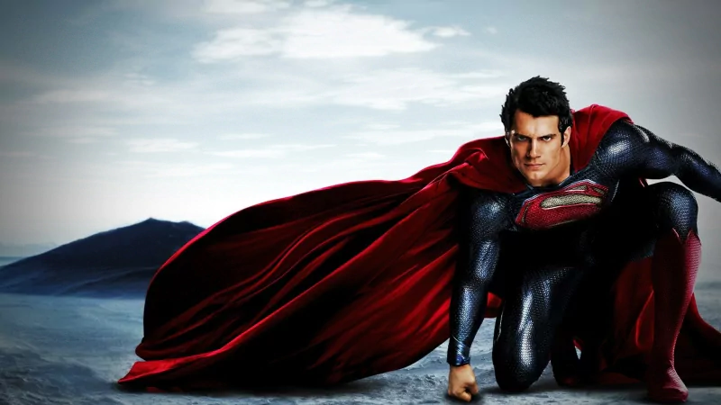 Henry Cavill as Superman in a dynamic pose from the movie Man of Steel, wearing the iconic blue suit and red cape against a cloudy sky background.