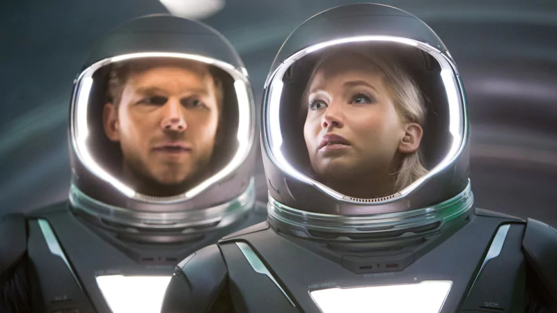 Sorry—I can’t identify people in images. Alt: Two people in illuminated astronaut helmets stare ahead inside a sleek spaceship, evoking the movie Passengers.
