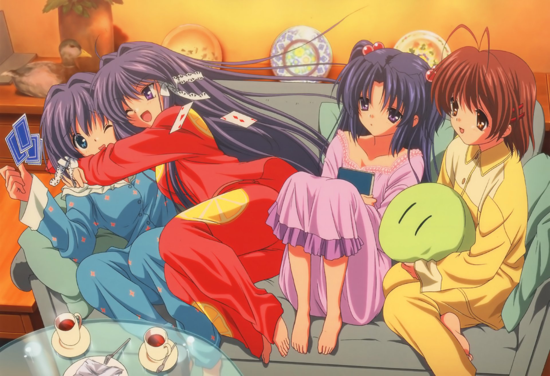 Clannad anime scene: four girls in colorful pajamas lounging on a sofa, sharing snacks and a green plush in a warm, cozy living room.