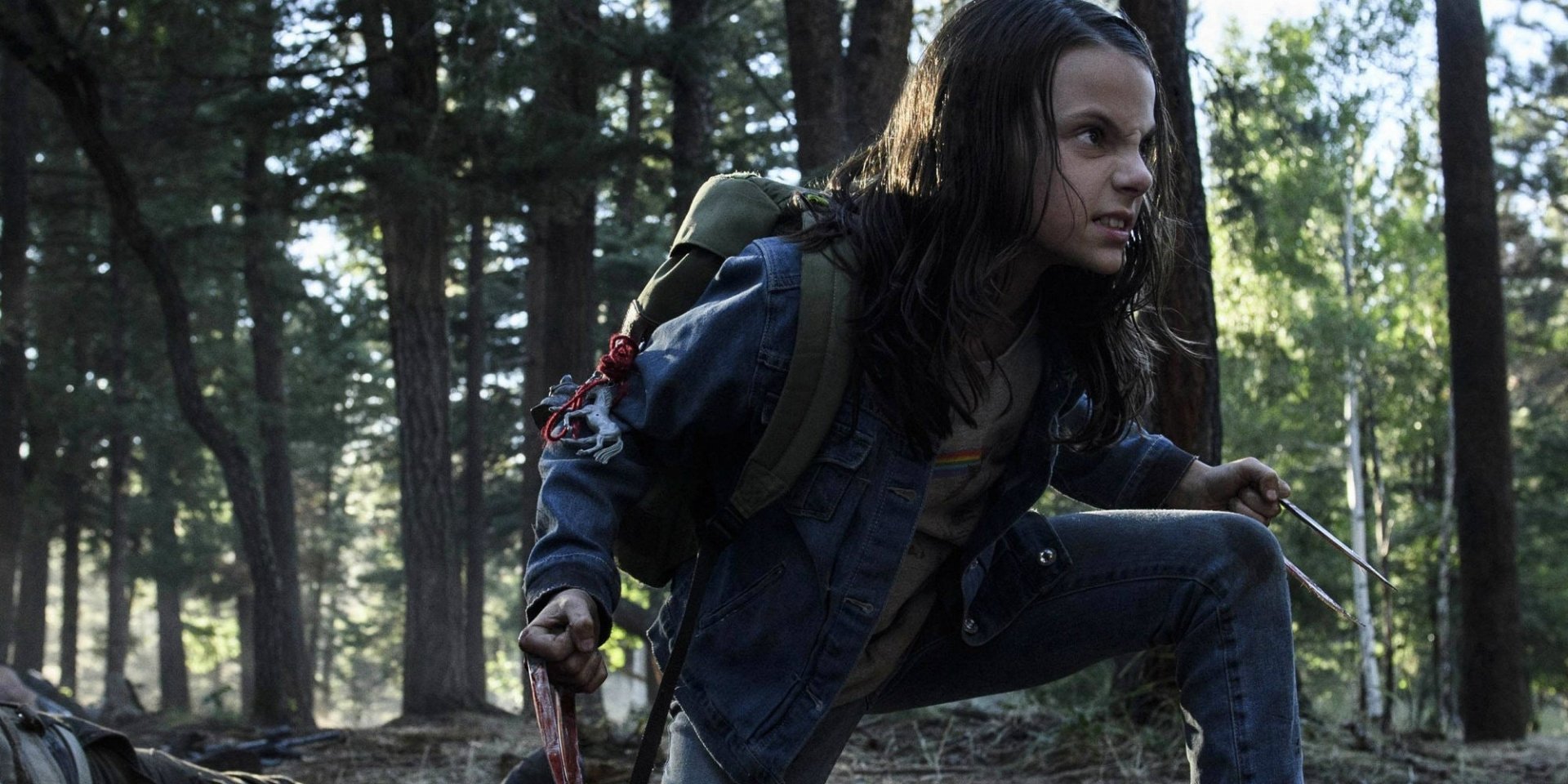 Girl crouches in a forest, backpack on and metal claws extended, tense and ready — a scene from the movie Logan.