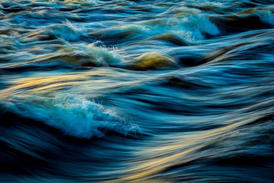 Close-up artistic view of blue water with paint-like textures and flowing waves illuminated by soft light.