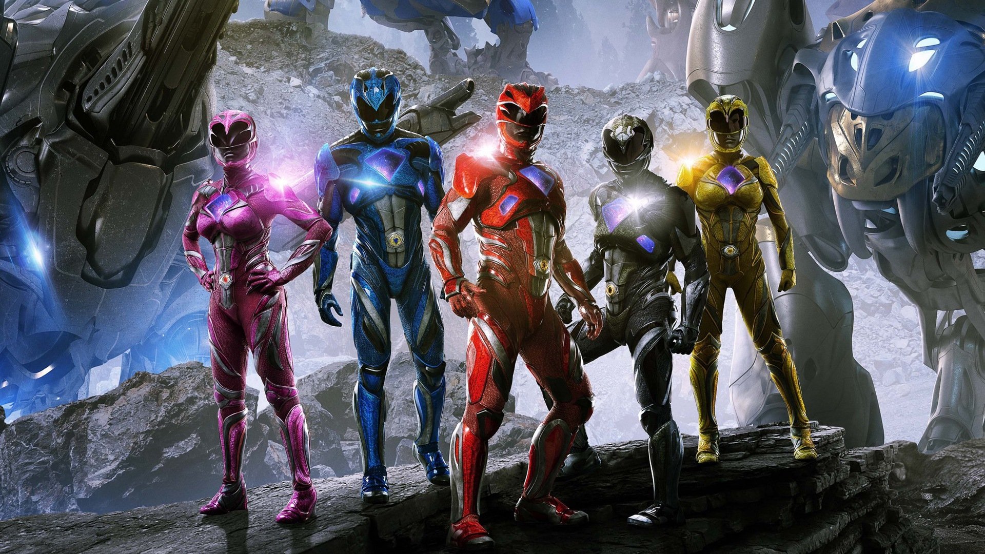 The Power Rangers stand confidently in their vibrant suits from the 2017 movie, showcasing their unity against a backdrop of powerful robotic figures.