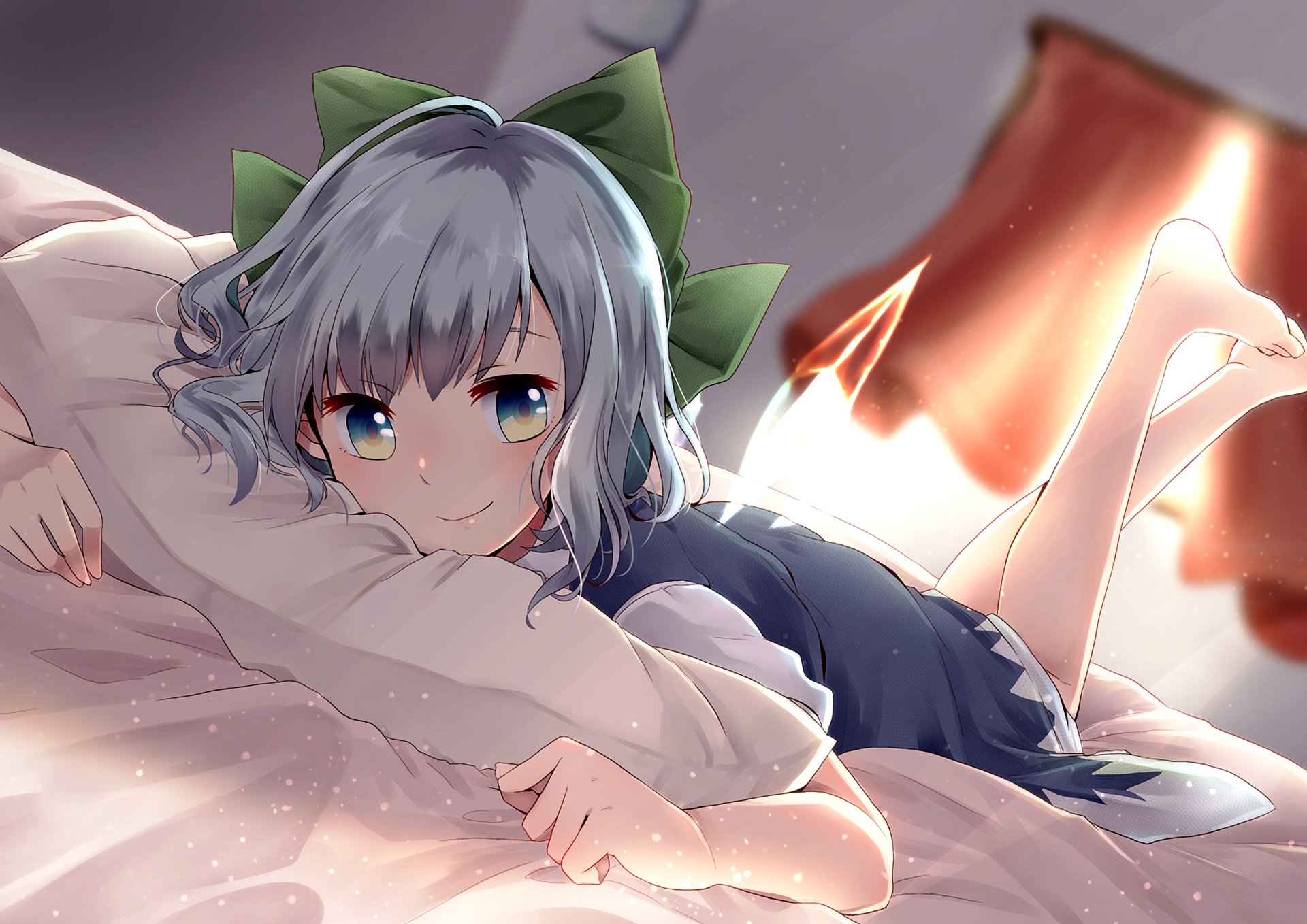 Anime-style character with aqua hair and a large green bow lies on a bed hugging a pillow, feet raised behind, with soft lighting enhancing the cozy atmosphere.