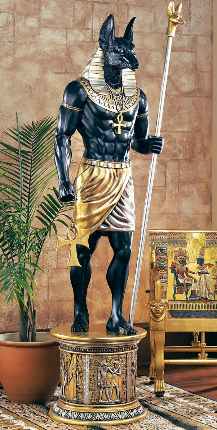 Fantasy Egyptian statue of a muscular Anubis-like jackal-headed god in gold kilt and ankh, holding a staff, standing on a carved pedestal beside an ornate throne and potted palm.