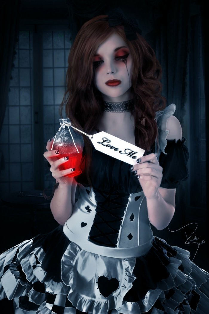 A dark, gothic woman in dramatic makeup and a black-and-white dress holds a vial of red liquid labeled Love Me against a shadowy, eerie background.