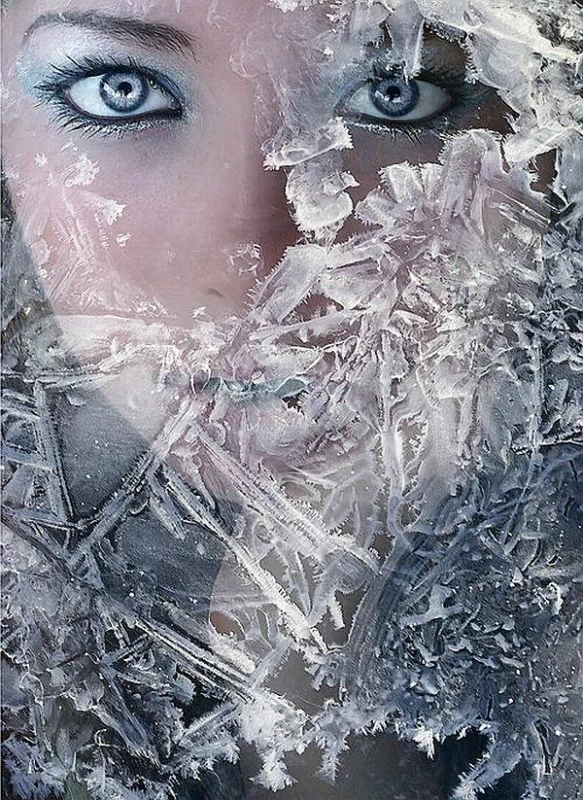 A striking artistic portrayal of a woman's face partially obscured by intricate ice patterns, highlighting her piercing blue eyes amidst a frozen backdrop.