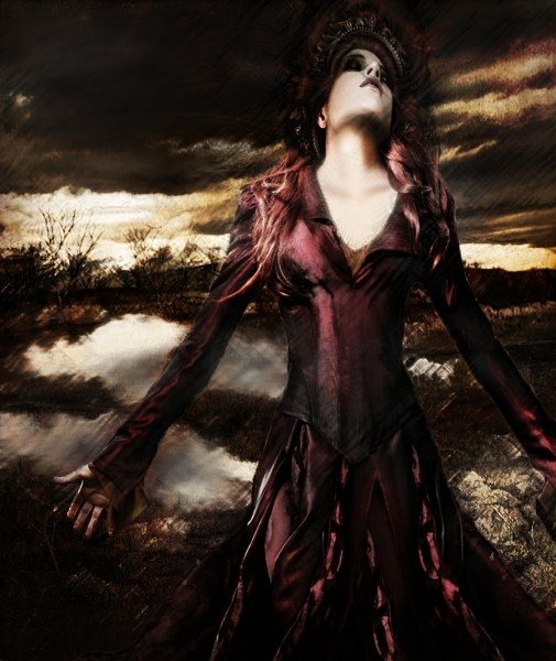 A gothic fantasy woman in a dark, flowing dress stands with arms outstretched against a stormy, dramatic sky near a reflective body of water.