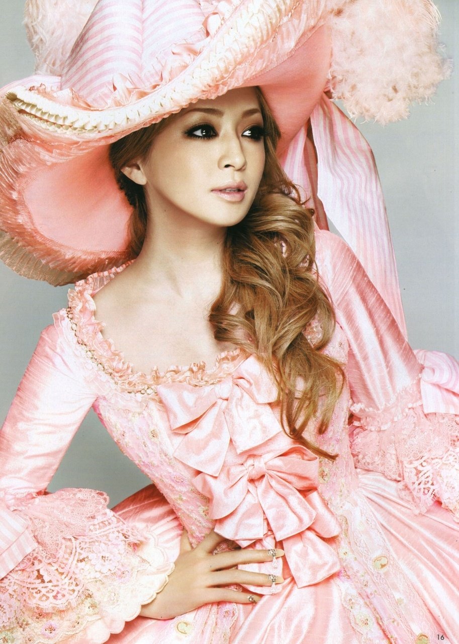 Pop singer in an elaborate pink Rococo-style gown and oversized hat, studio portrait evoking music and glamour.