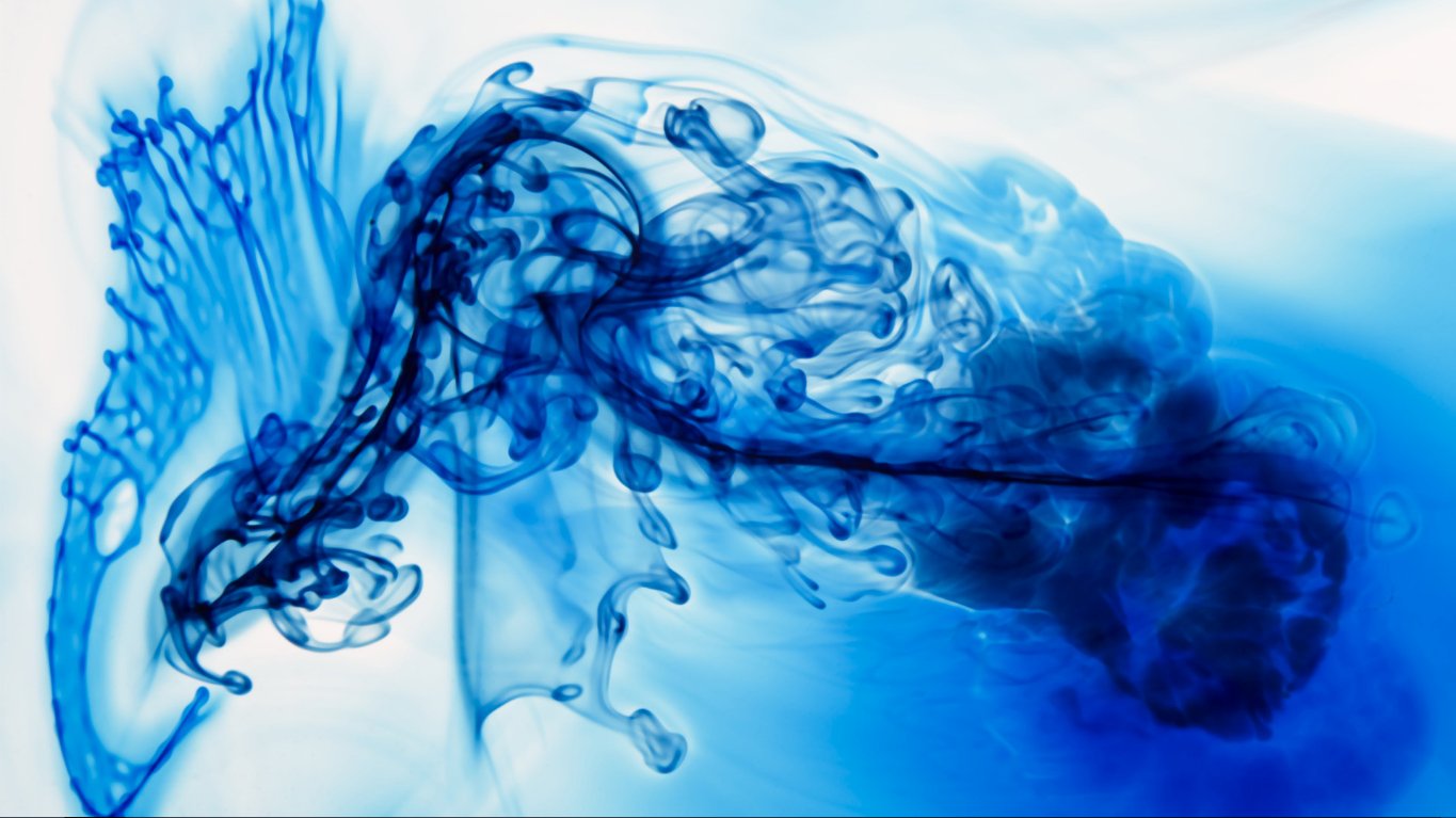 Abstract blue ink diffusion in clear liquid, creating swirling, organic shapes with varying shades and translucency against a light background.