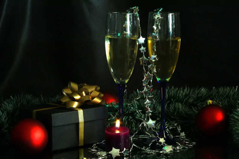 Two champagne flutes sparkle amid a festive setting of red ornaments, a gift box, and a candle, capturing the joyful spirit of a Christmas holiday celebration.