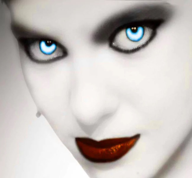 A striking close-up of a vampire figure with pale skin, dark makeup, and piercing blue eyes, exuding a dark and mysterious aura. The lips are painted a deep, glossy red.