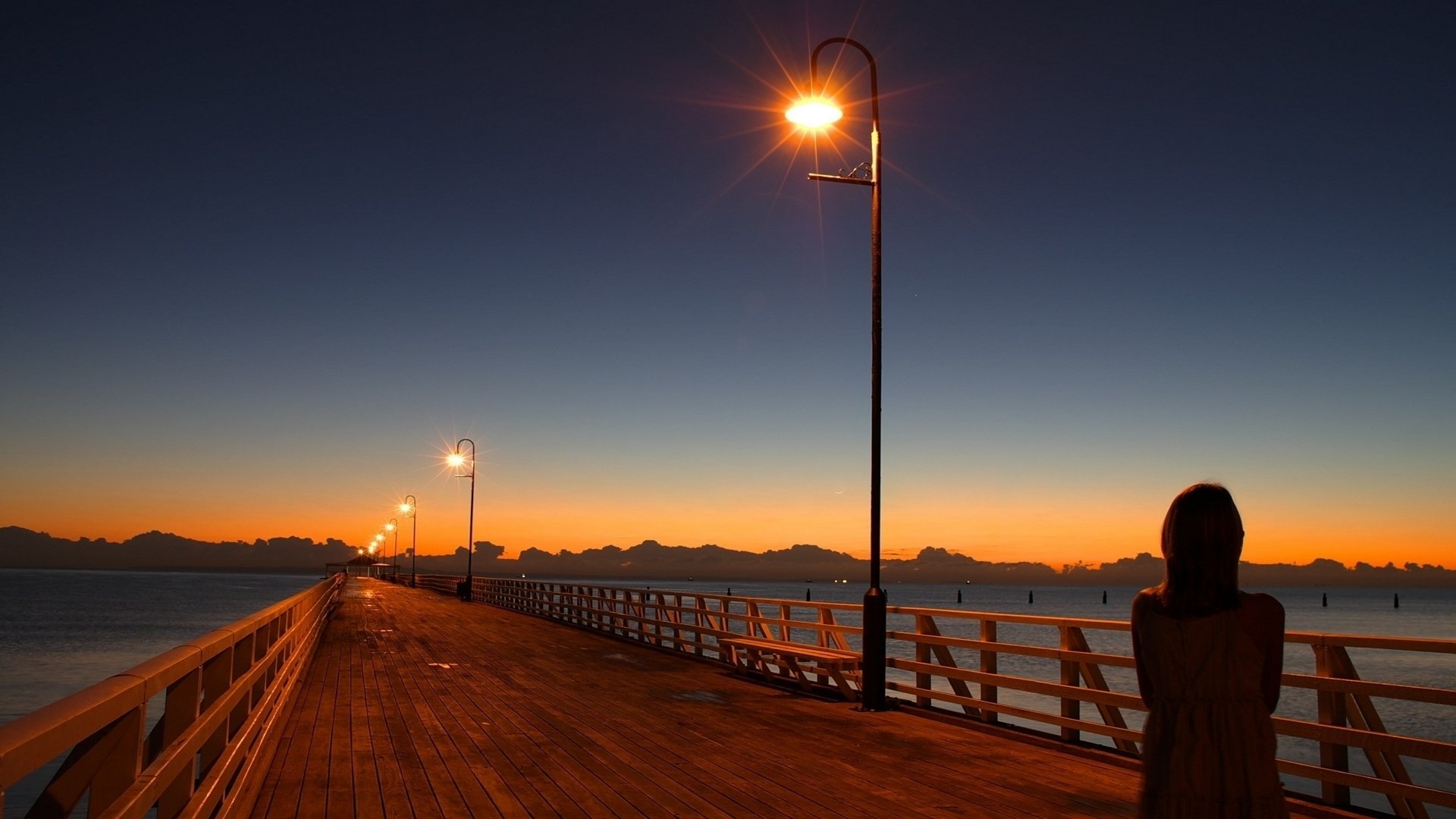 Cinematic photography of a wooden pier at dusk, warm lamplight bathing the boards and a lone silhouette, conjuring Rapture (Bioshock) atmosphere.