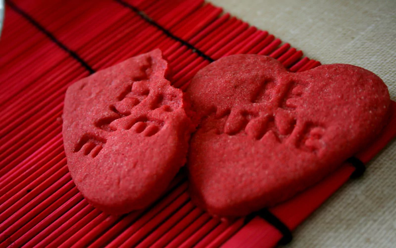Two red heart-shaped cookies with Be Mine written on them, resting on a red bamboo mat, celebrating Valentine's Day.