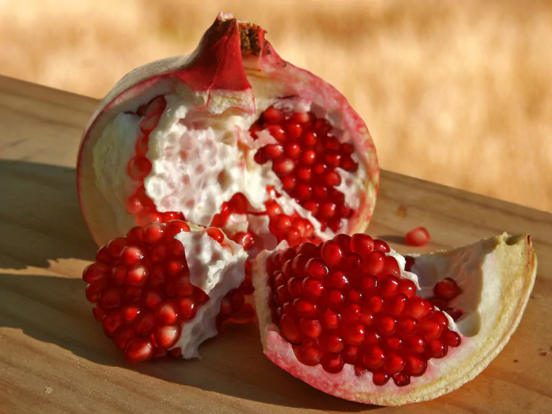 A pomegranate fruit with bright red seeds displayed on a wooden surface, highlighting its vibrant and juicy food contents.