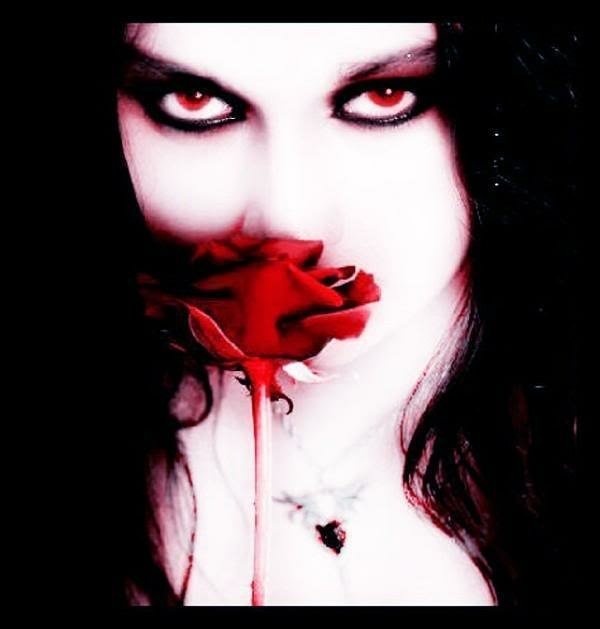 A dark, gothic portrait of a pale person with striking red eyes holding a vivid red rose close to their face, contrasting sharply with the black background and hair.
