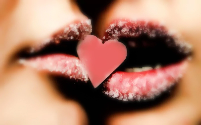 Close-up of two lips with a frosty edge, almost touching, and a pink heart between them, capturing an artistic expression of love.