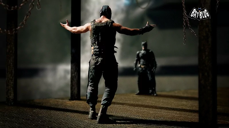 Scene from the movie The Dark Knight Rises: Bane, arms outstretched, confronts a dark-clad Batman in a shadowy, industrial chamber.