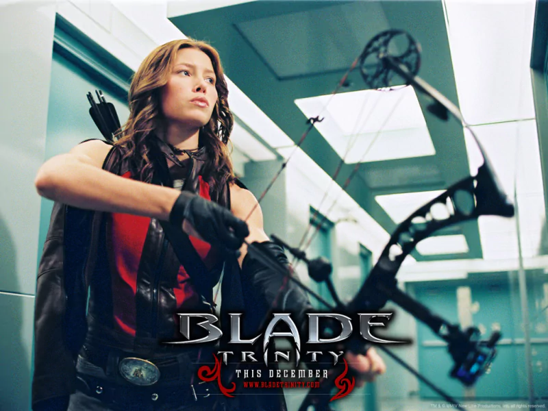 Jessica Biel as an archer in the movie Blade: Trinity, aiming a bow with focused intensity in a modern, glass-paneled setting.