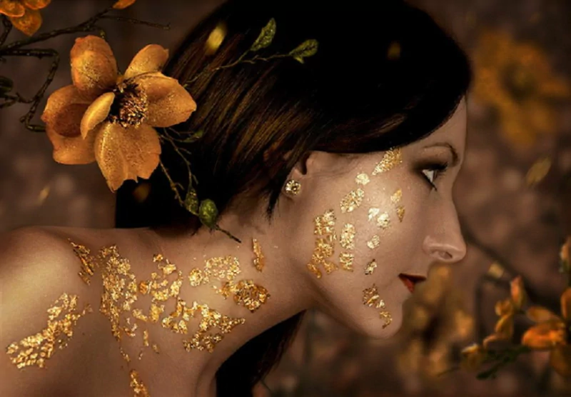 Brunette woman adorned with gold accents and vibrant red lips poses amid sparkling flowers, radiating elegance and beauty in a captivating, artistic composition.