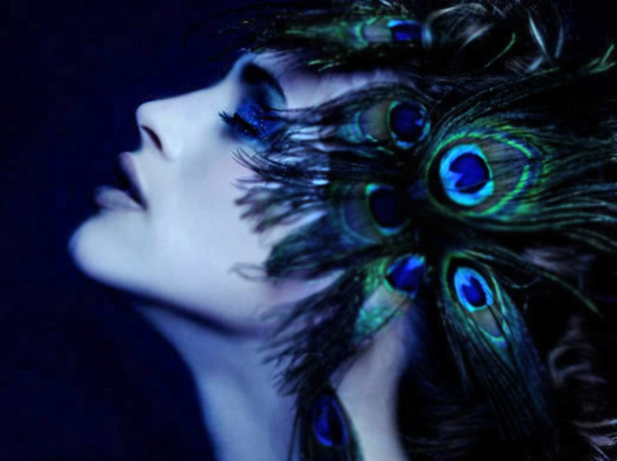 A beautiful woman adorned with vibrant peacock feathers gazes gracefully to the side, showcasing the stunning colors and intricate patterns of the feathers against a dark background.