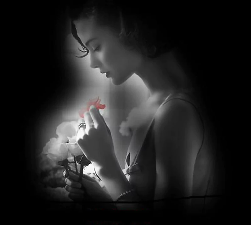 A pensive woman in soft black and white holds a flower, a ring on her finger, evoking emotions of sadness and contemplation in this striking photograph.