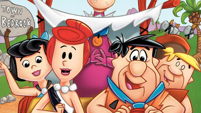 The Flintstones TV show: Fred, Wilma, Betty and Barney pose together in colorful Bedrock beside a Town of Bedrock sign.