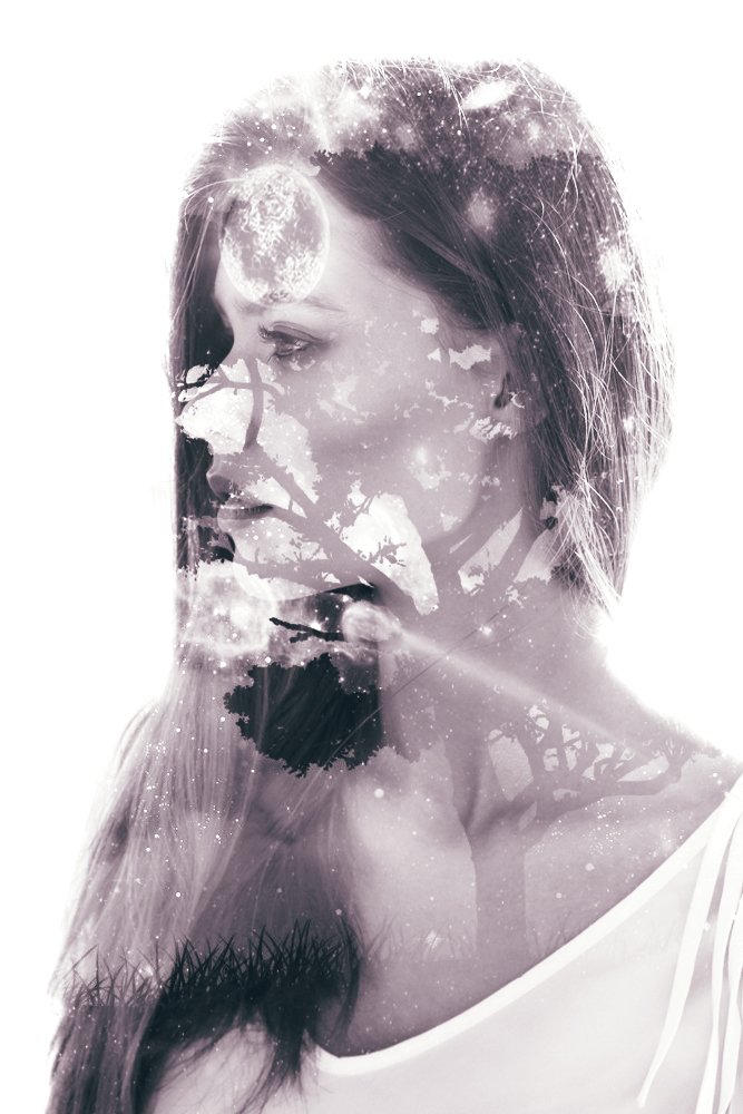 Artistic double exposure of a woman’s profile blended with tree branches and abstract light textures in soft monochrome tones.