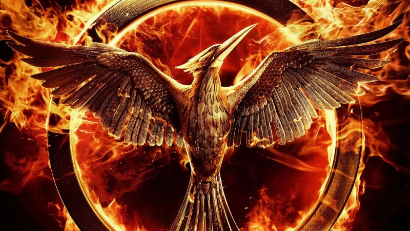 Fiery Mockingjay emblem — a metallic bird with outstretched wings inside a ring of flames, promotional image for the movie The Hunger Games: Mockingjay - Part 1.