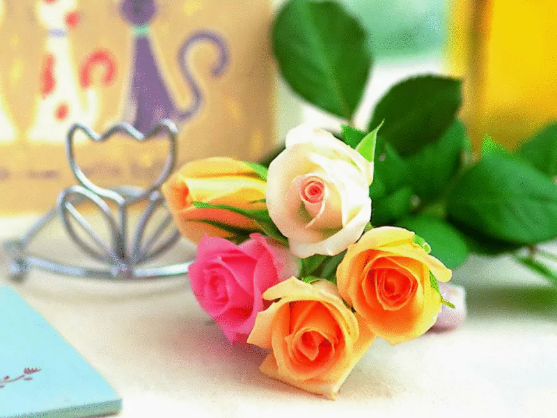 A vibrant bouquet of multi-colored roses—pink, orange, and white—sits gracefully among green leaves, showcasing the beauty of nature with a soft, blurred background.