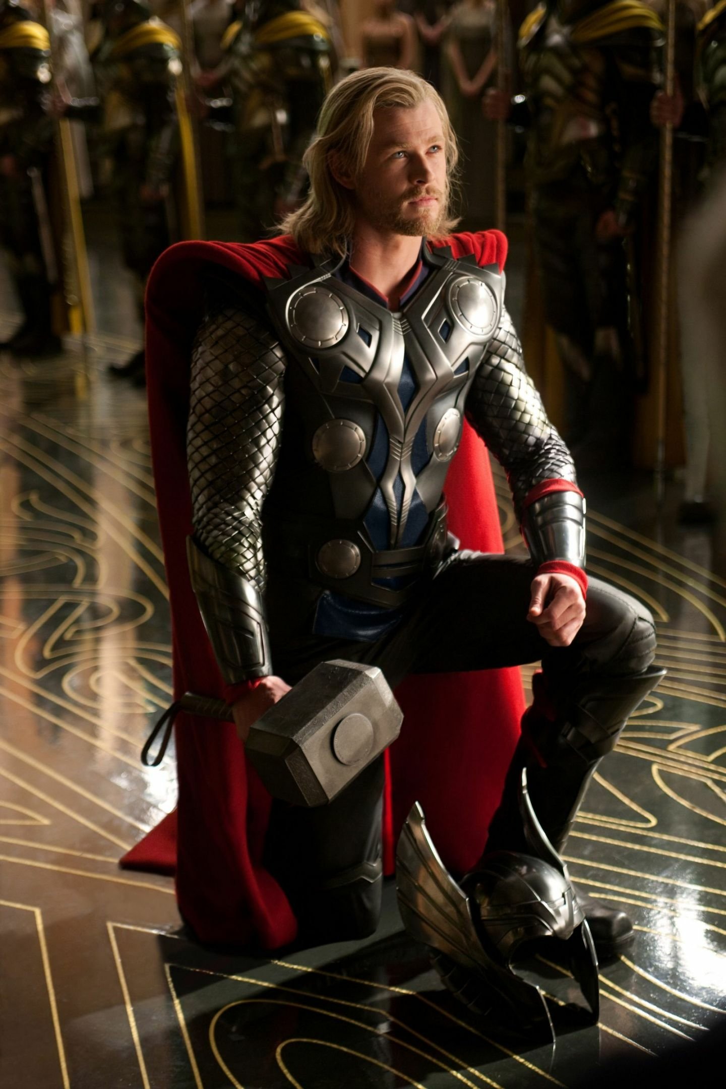 Thor, the movie character, kneels holding his hammer in a detailed armor suit and red cape, set against an ornate background with figures standing behind him.
