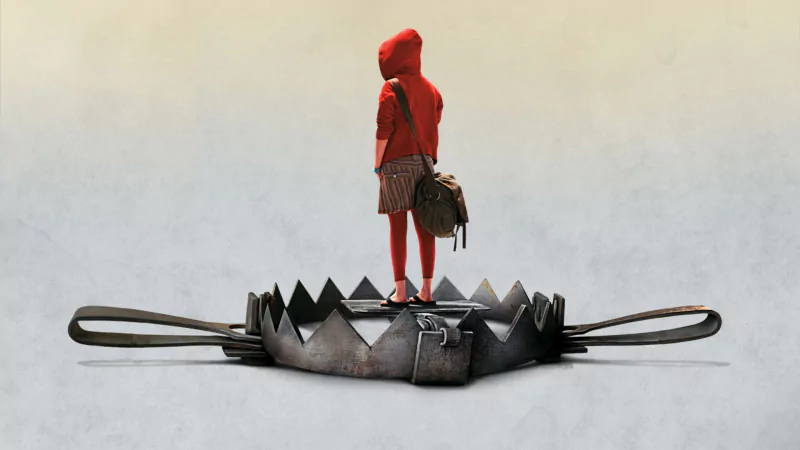Photography, manipulation: a lone figure in a red hooded coat and skirt stands on an oversized metal bear trap, clutching a satchel against a muted, surreal backdrop.