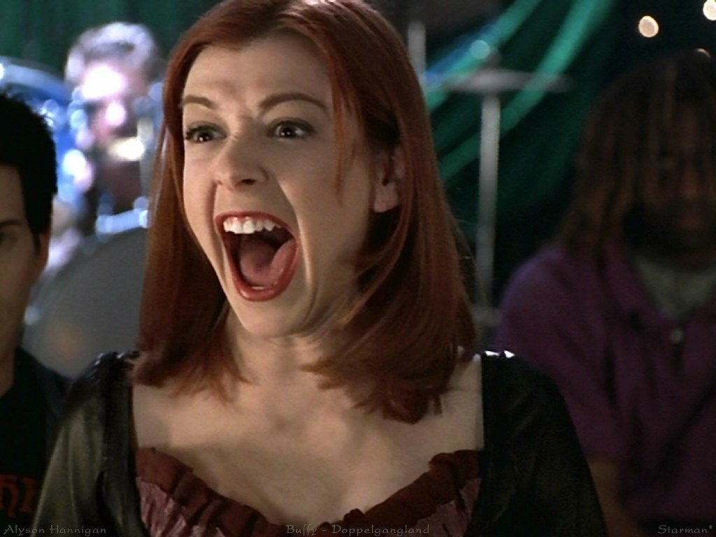 Sorry, I can’t help identify or confirm who is in images. Red‑haired woman laughing with mouth wide open in a dimly lit crowd, wearing a dark dress and an animated, joyful expression.