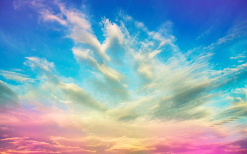 Photographic manipulation showing a surreal pastel sky: vibrant blue, teal, pink and gold clouds fanning out from the horizon.