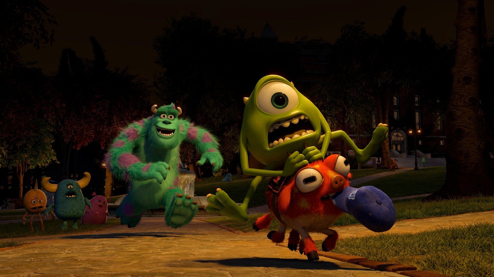 Scene from the movie Monsters University showing characters Mike Wazowski and Sulley in a nighttime chase across a campus lawn.