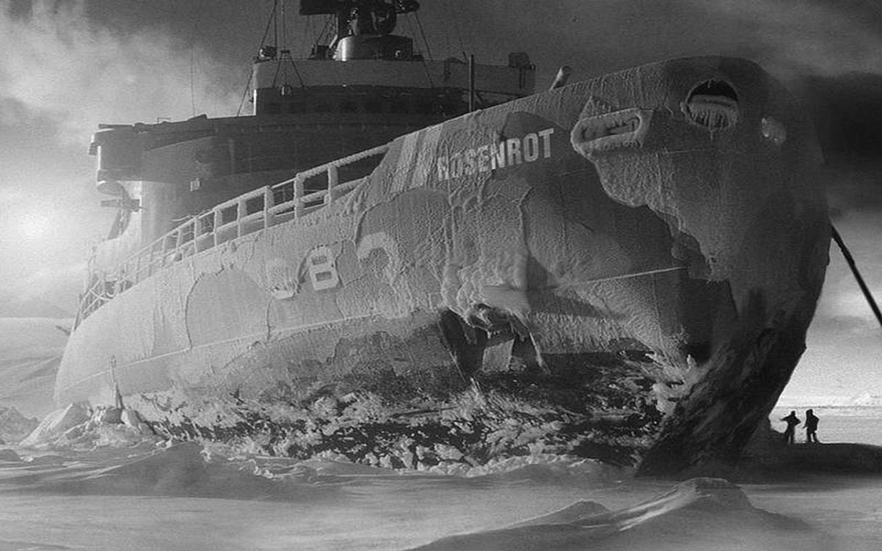 Black-and-white photo of the icebound ship Rosenrot stuck in a frozen sea; two tiny figures at the bow evoke stark Rammstein music imagery.