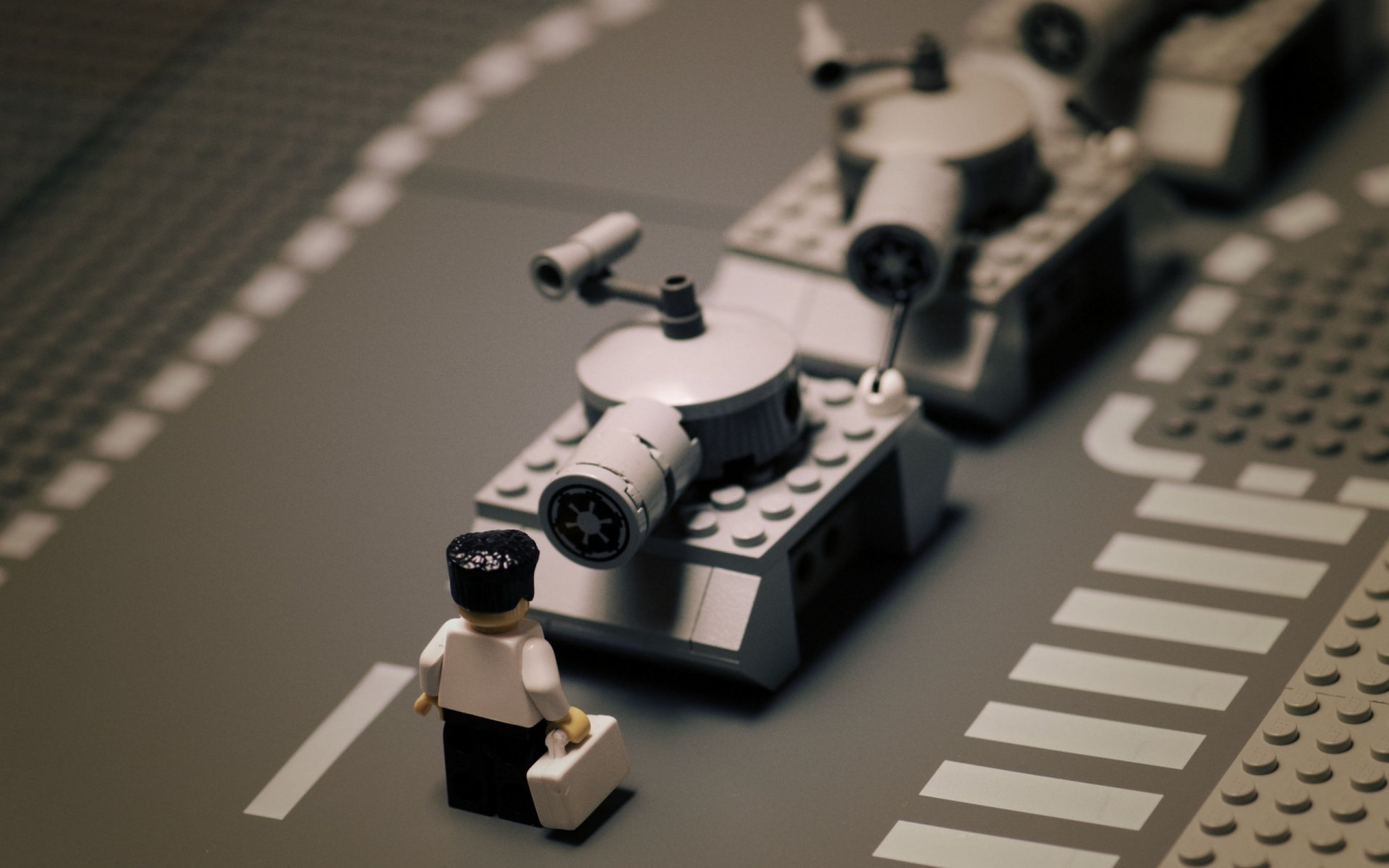 A man-made LEGO scene showing a small LEGO figure standing next to a LEGO vehicle on a gray road with crosswalk markings.