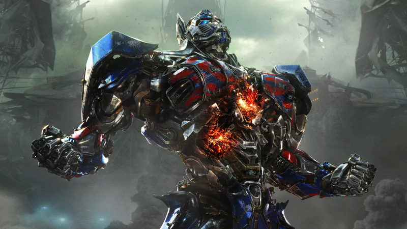 Optimus Prime from the movie Transformers: Age of Extinction stands battle-worn with glowing damage on his chest, surrounded by a smoky, war-torn environment.
