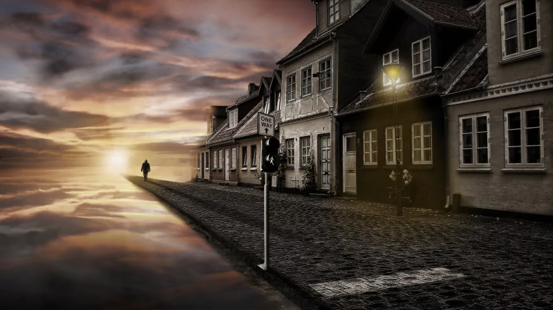 Abstract and artistic image of a cobblestone street with old buildings fading into a cloudy sky at sunset, featuring a lone figure walking toward the horizon.