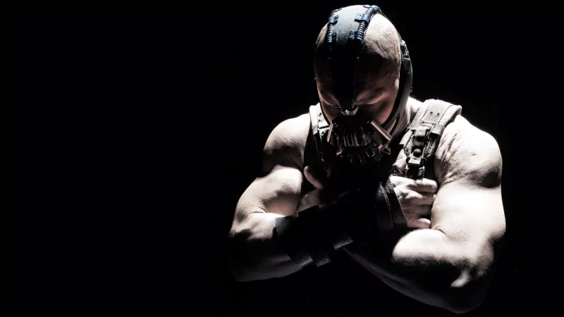 Bane, a muscular character wearing a distinctive mask, appears in a dark setting from the movie The Dark Knight Rises.