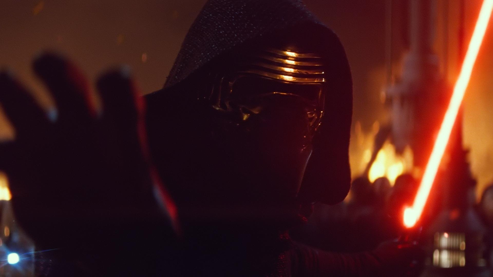 Hooded Kylo Ren brandishing his red crossguard lightsaber amid fire and smoke — scene from Star Wars Episode VII: The Force Awakens.