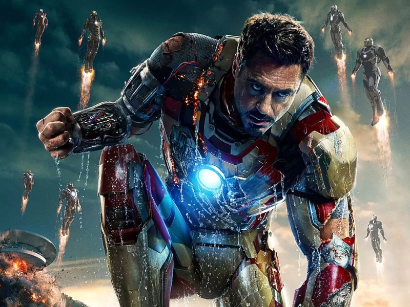 Battle-damaged Iron Man crouches with a glowing arc reactor as multiple armored suits fly overhead — a dramatic scene from the movie Iron Man 3.