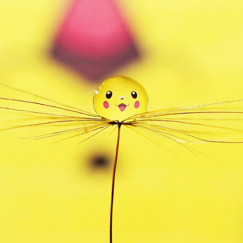 A close-up of a water droplet on a seed, reflecting Pikachu’s yellow face from the Pokémon video game series against a soft yellow background.