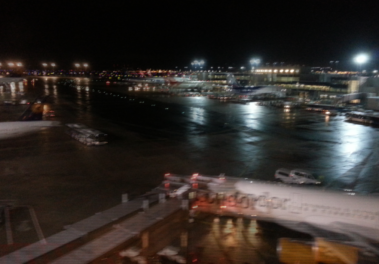 A nighttime view of Fraport airport, featuring interlaced 3D reflections on wet pavement and illuminated aircraft, showcasing the man-made structure in a bustling atmosphere.