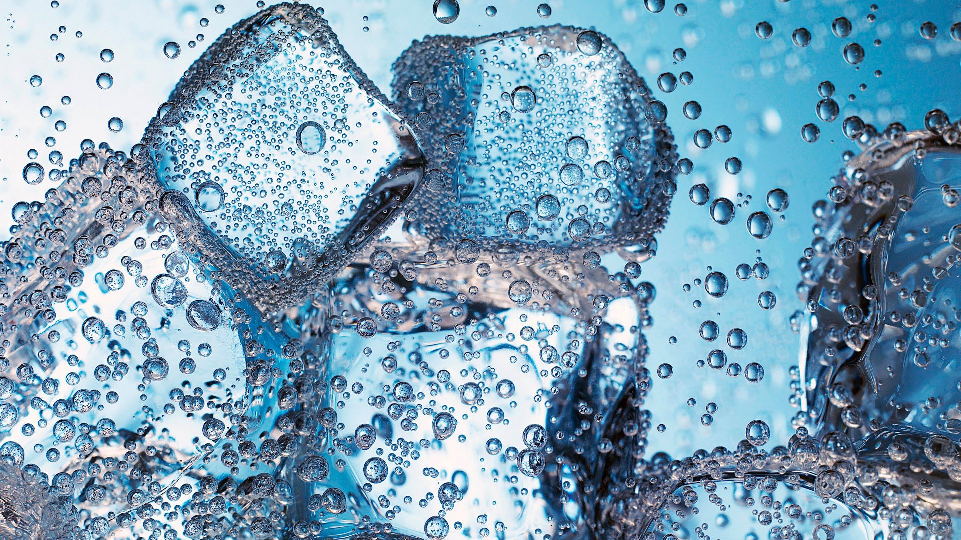 Close-up photography of an ice cube surrounded by water splashes and bubbles, crystalline edges and droplets suspended against a cool blue background.