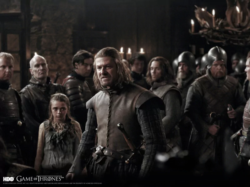 Scene from Game of Thrones featuring Sean Bean as Eddard Stark and Maisie Williams as Arya Stark surrounded by soldiers in a dimly lit hall.