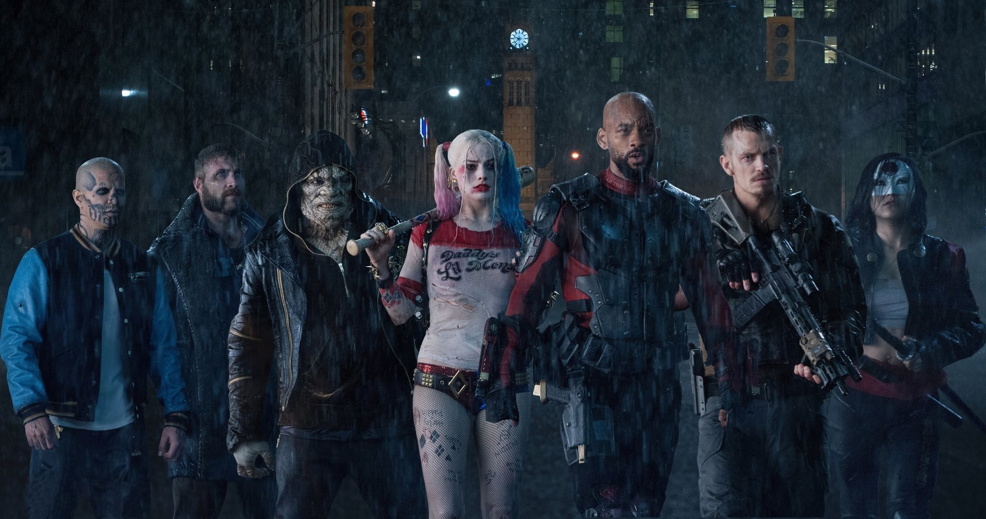 Suicide Squad movie still: Harley Quinn, Deadshot, Captain Boomerang, Killer Croc and others stand together in the rain, weapons ready.