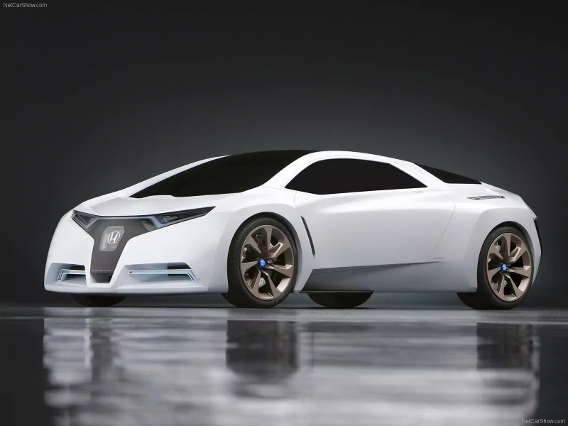 White Honda FC Sport concept vehicle with a low, futuristic coupe profile, blacked windows, angular LED headlights and bronze-accent wheels reflected on a glossy studio floor.