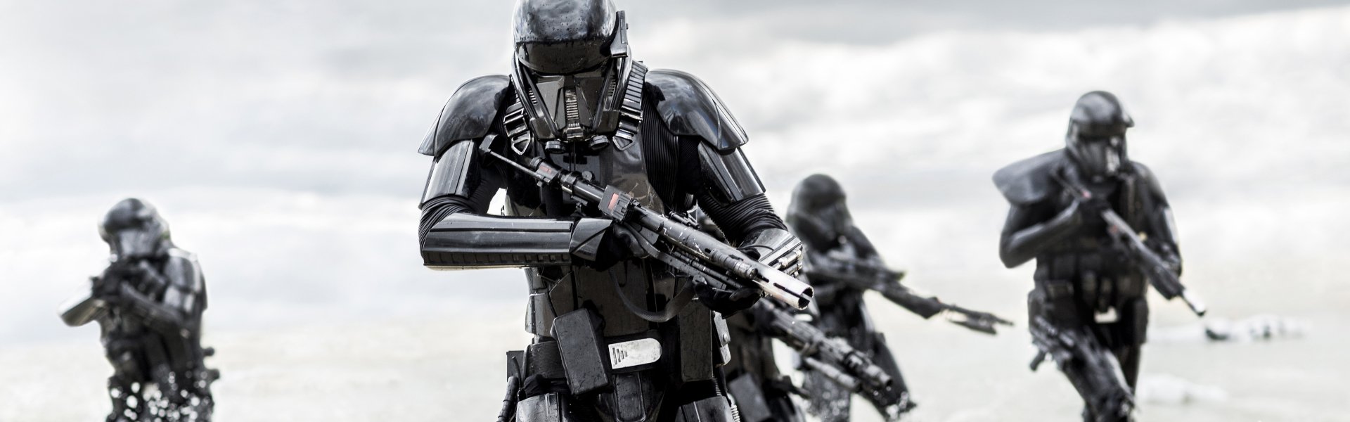 Imperial Death Troopers in black armor march across a bleak field, rifles at the ready — scene from Rogue One: A Star Wars Story.