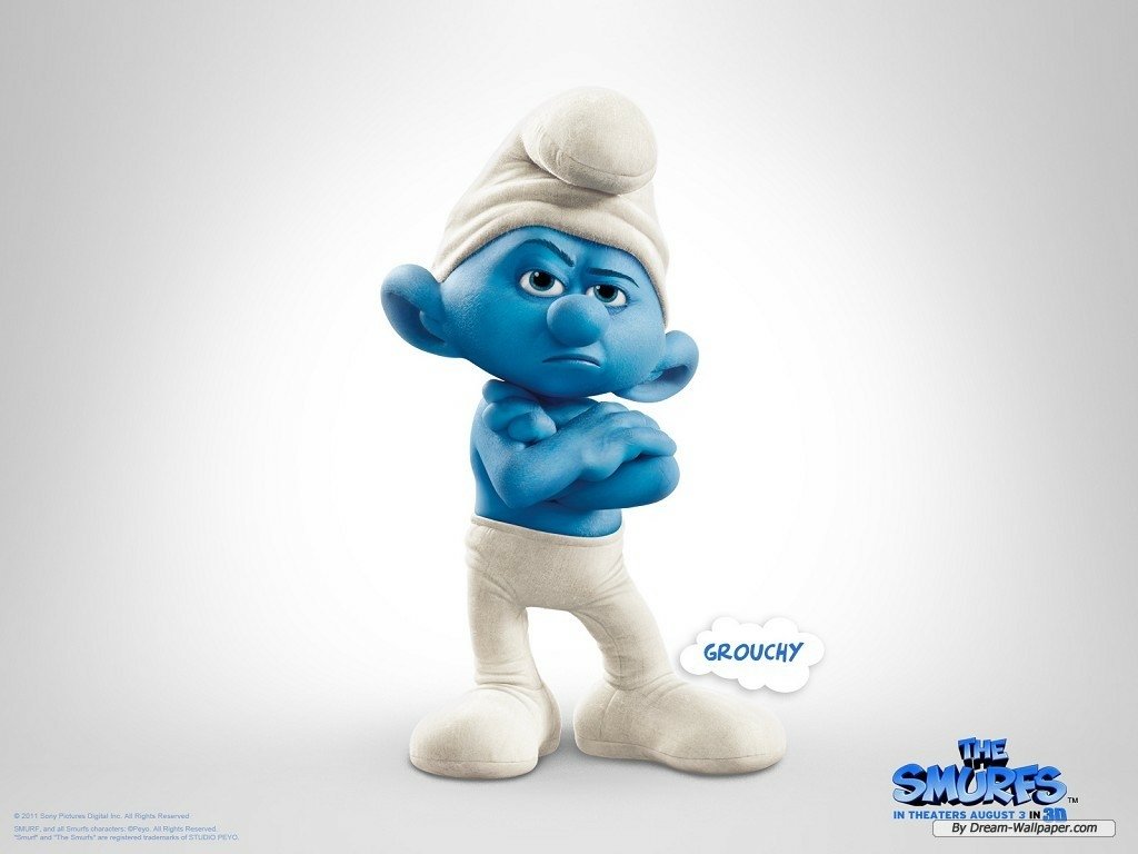 Grouchy Smurf from the movie The Smurfs stands with arms crossed, scowling, wearing a white hat and pants against a plain light background.